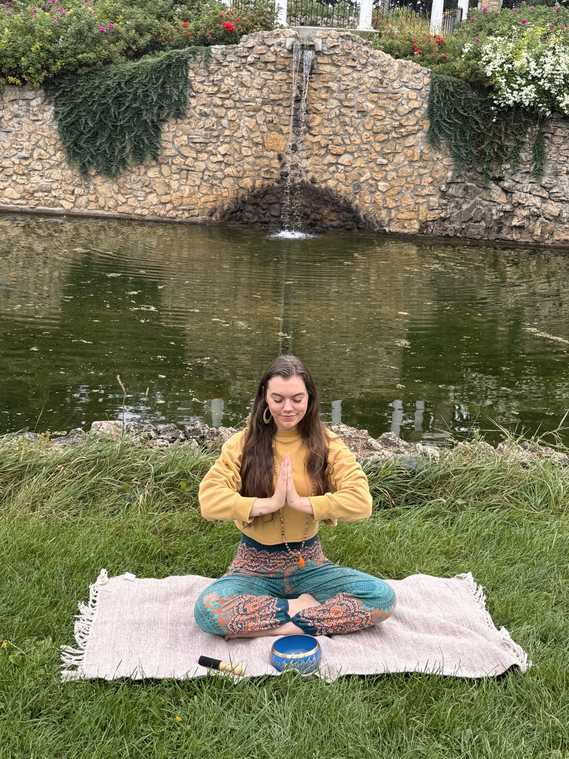 Maria Feider sitting outdoors in a peaceful wellness setting near water and nature